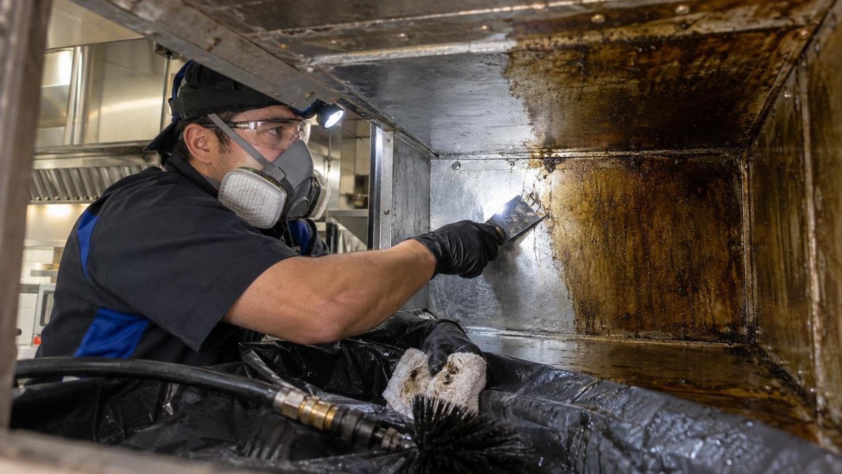 Technician cleaning accumulated grease from a commercial kitchen exhaust duct